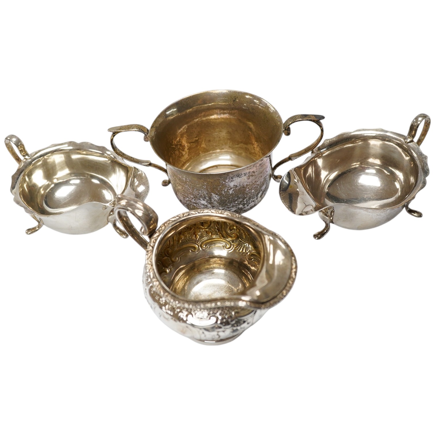 A George III Scottish silver cream jug, later embossed, a pair of George V silver sauce boats and an Edwardian hammered silver two handled porringer, by Moss Morris,18.4oz. Condition - poor to fair